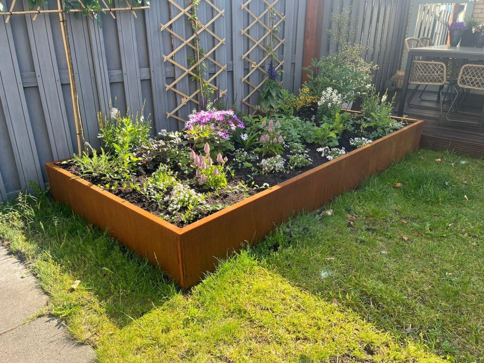 Verhoogde tuinborder met cortenstalen randen en bloeiende beplanting